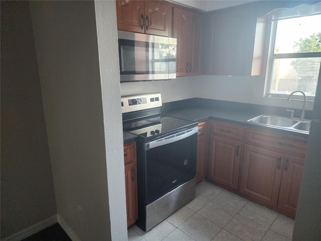 A kitchen features wood cabinets, stainless steel appliances, a black countertop, and a tile floor — 7210 N MANHATTAN AVENUE UNIT 1821, TAMPA, FL