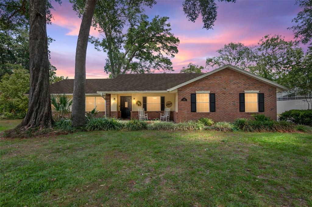 A single-story brick house with a front porch sits on a grassy lawn at sunset — 986 SE 57TH AVENUE, OCALA, FL