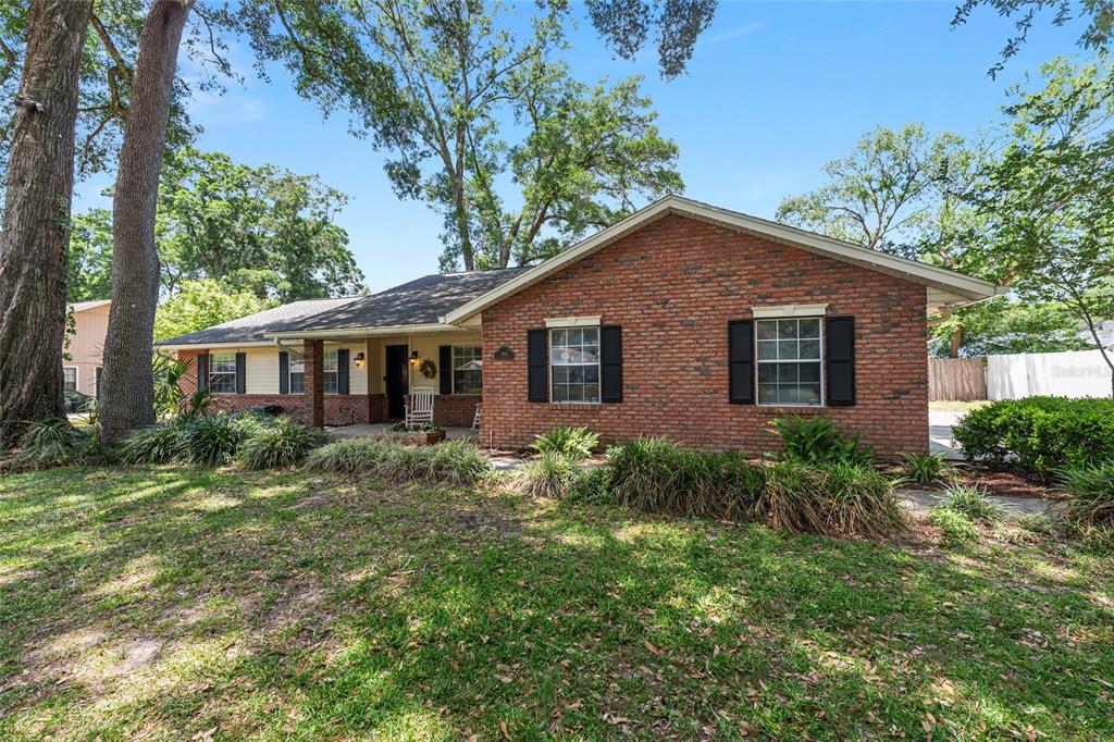 A single-story brick house with a covered entryway and black shutters sits on a lawn — 986 SE 57TH AVENUE, OCALA, FL