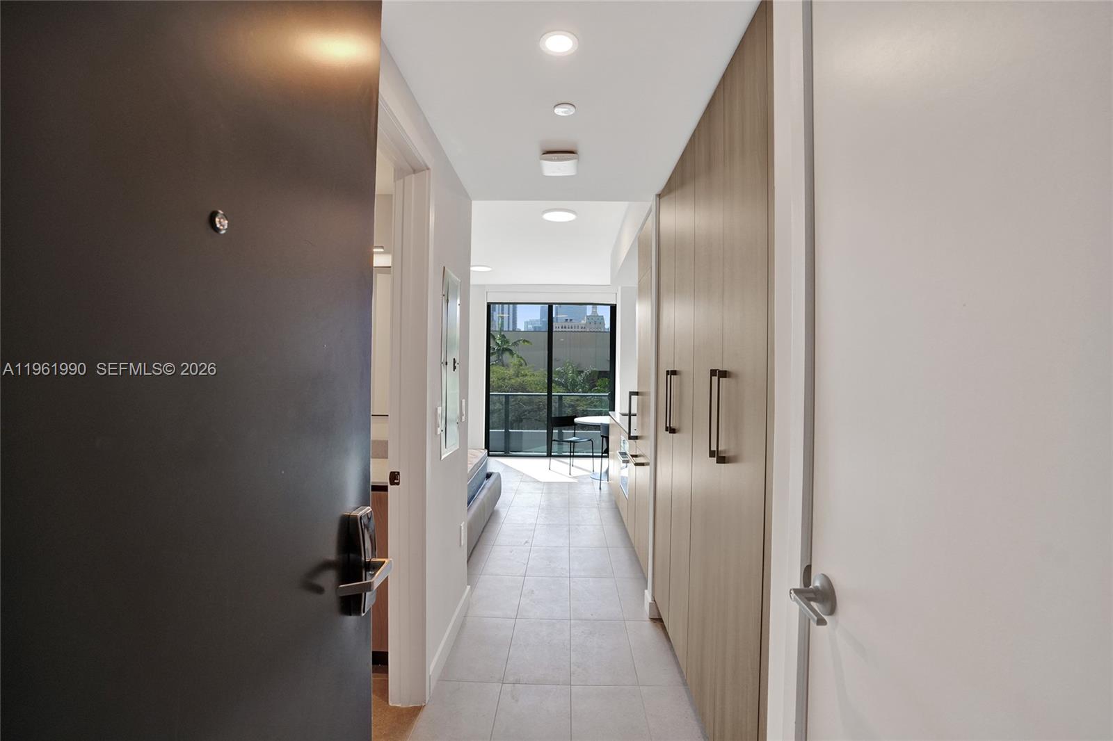 A hallway with light tile flooring leads past built-in wood cabinetry toward a balcony window — 121 NE 5th Street # 401B, Miami FL 33132, MIAMI, FL