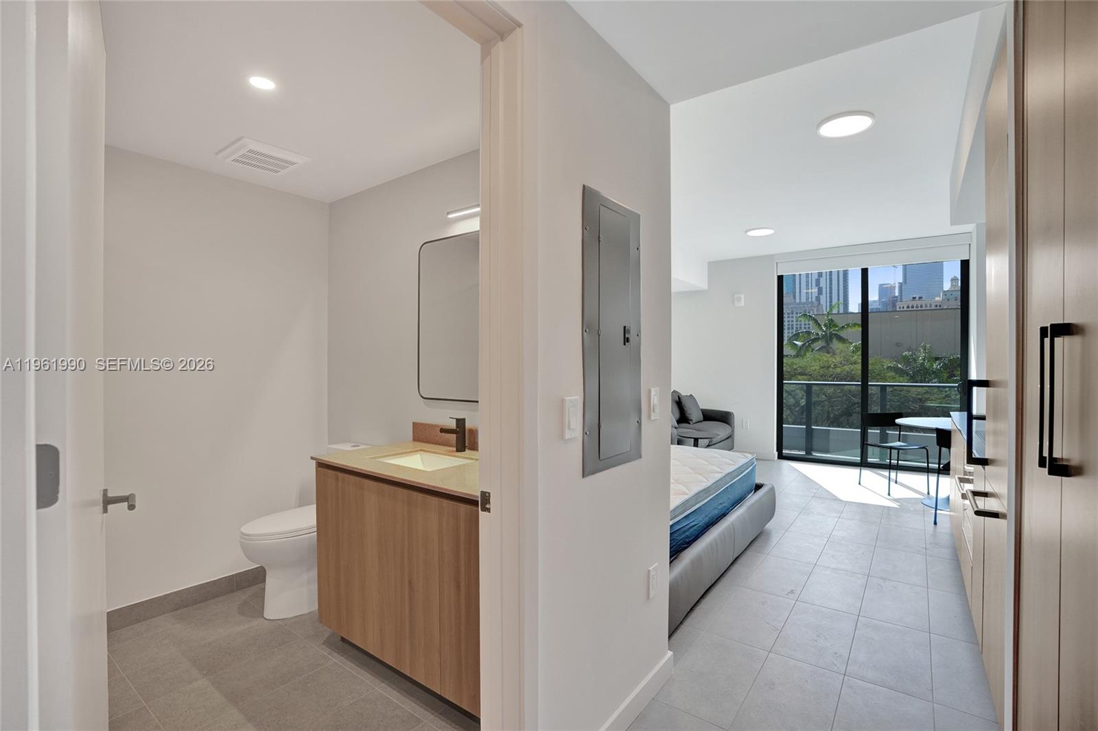 A bathroom with wood cabinetry opens into a bedroom with a balcony and city view — 121 NE 5th Street # 401B, Miami FL 33132, MIAMI, FL