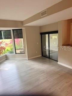 A living room with light wood-look flooring, a large window, and sliding glass patio doors — 485 WESTLAKE BOULEVARD UNIT 70, PALM HARBOR, FL