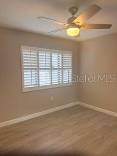 An empty bedroom features light-colored wood-look flooring, beige walls, a ceiling fan, and plantation shutters — 485 WESTLAKE BOULEVARD UNIT 70, PALM HARBOR, FL