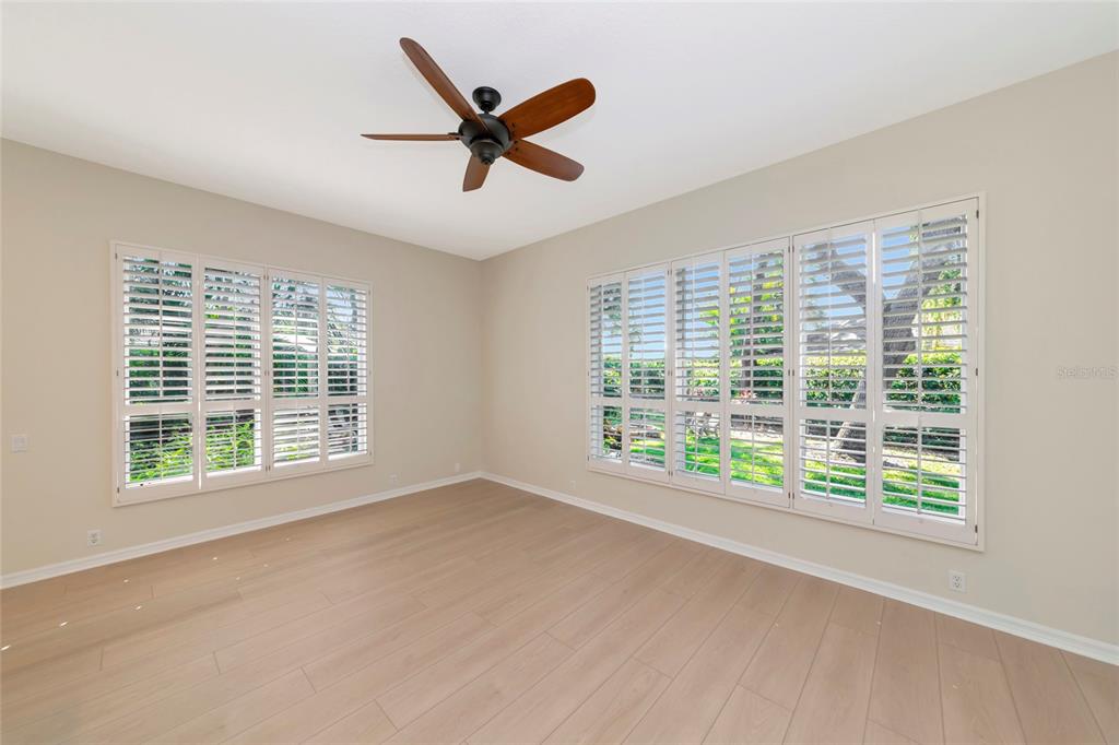 An empty room with light wood-look flooring, a ceiling fan, and white plantation shutters — 309 AMERICAS CUP BOULEVARD, BRADENTON, FL
