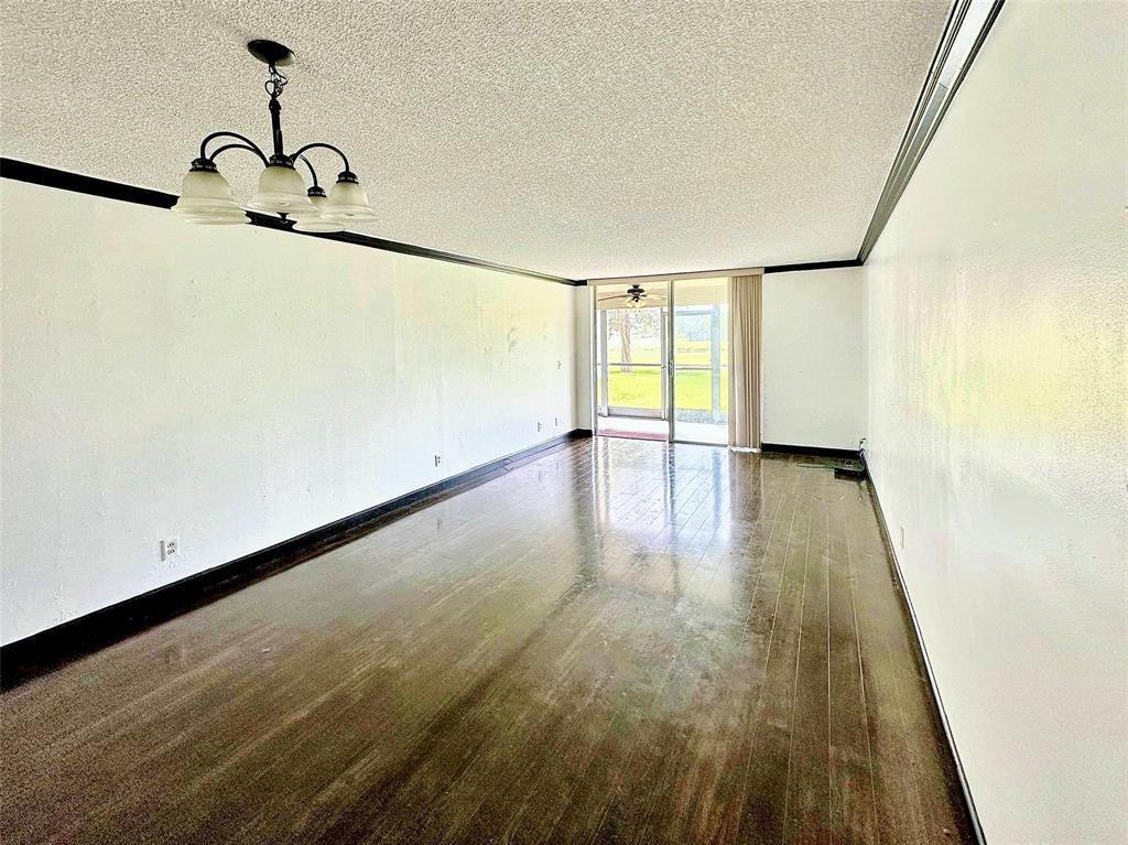 An empty living room features dark wood flooring, white walls with black trim, and a chandelier — 3231 Holiday Springs Boulevard # 105, Margate FL 33063, MARGATE, FL