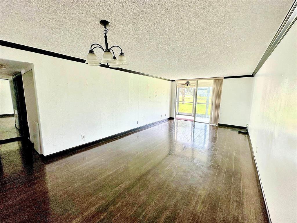 An empty living room features dark wood flooring, white walls, and a hanging light fixture — 3231 Holiday Springs Boulevard # 105, Margate FL 33063, MARGATE, FL