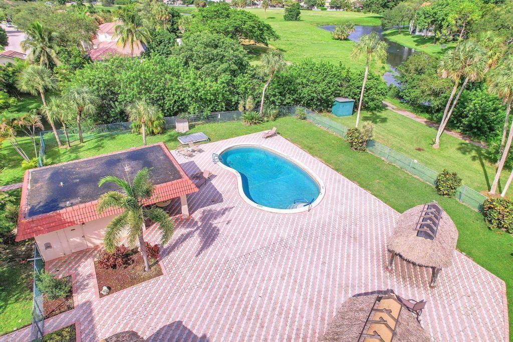 An aerial view of a backyard featuring a swimming pool, patio, and two tiki huts — 3231 Holiday Springs Boulevard # 105, Margate FL 33063, MARGATE, FL
