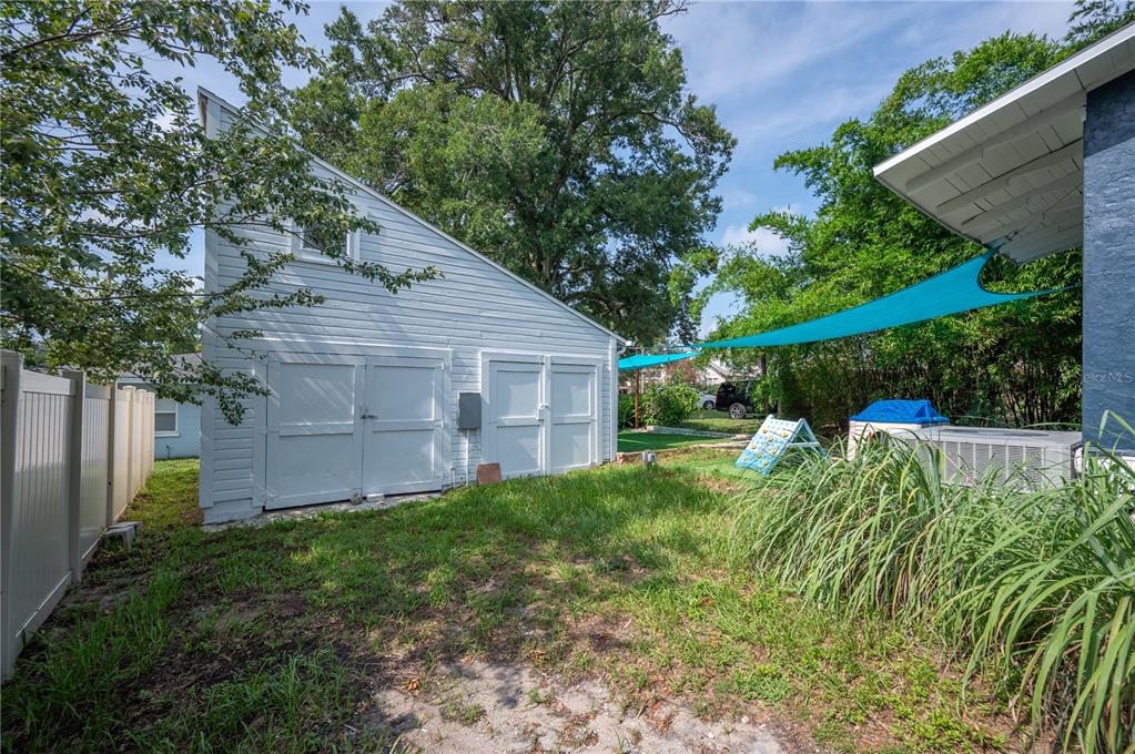 A backyard view showing a white shed with double doors and a blue shade sail — 817 E LIME STREET, LAKELAND, FL
