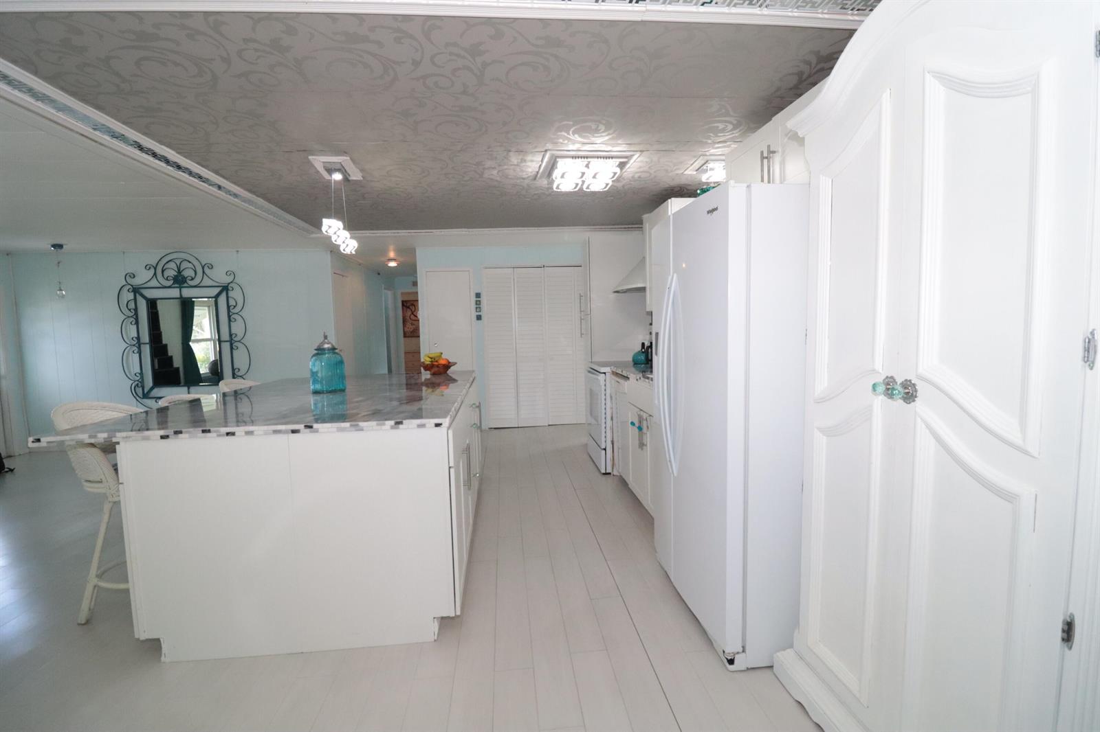 A white kitchen features a marble-topped island, light wood flooring, and a patterned ceiling — 1011 Andros, Boynton Beach FL 33436, BOYNTON BEACH, FL