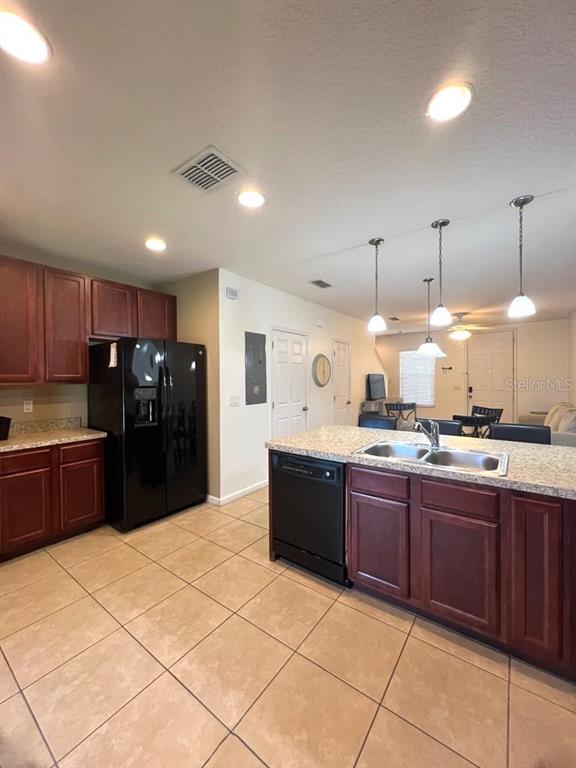 A kitchen features dark wood cabinets, a black refrigerator, a granite island, and tile flooring — 1162 CHELSEA DRIVE, DAVENPORT, FL