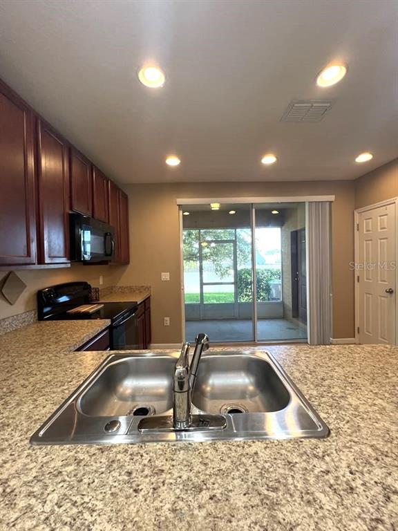 A kitchen features dark wood cabinets, granite countertops, a double sink, and a sliding glass door — 1162 CHELSEA DRIVE, DAVENPORT, FL