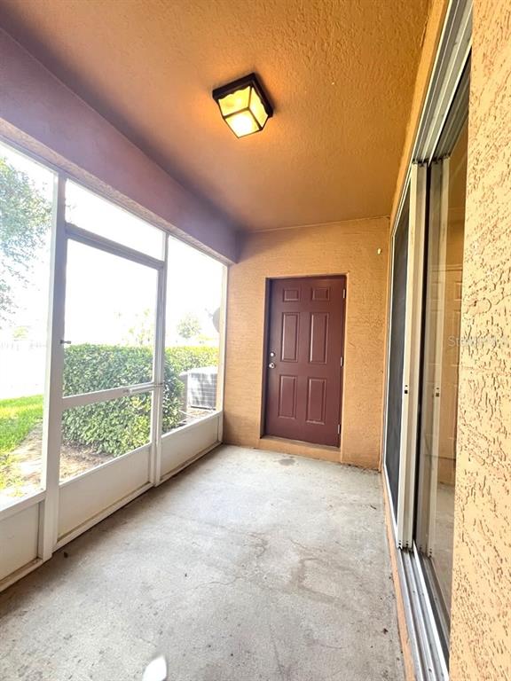 A screened-in patio features a concrete floor, a brown door, and a ceiling light fixture — 1162 CHELSEA DRIVE, DAVENPORT, FL