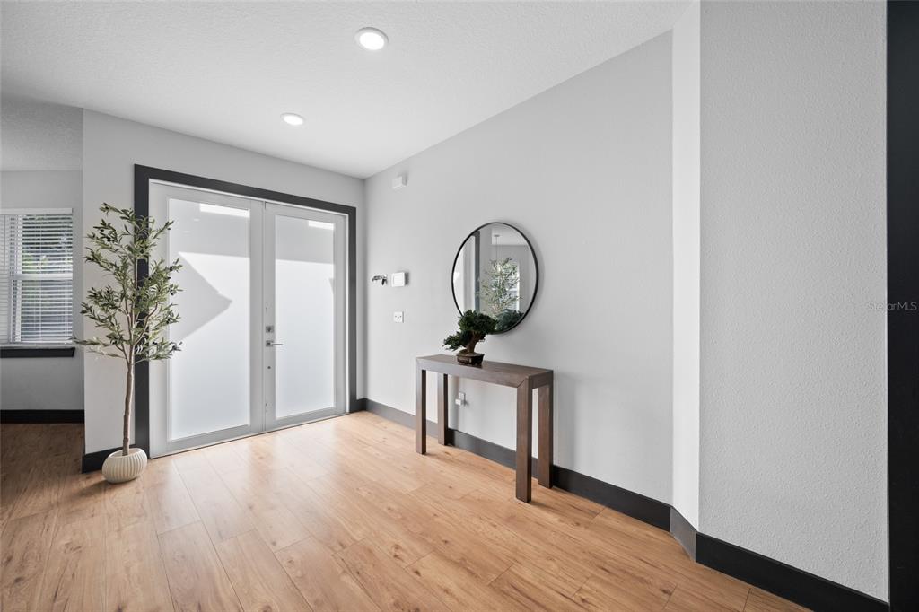A modern entryway features light wood flooring, white walls, a console table, and double glass doors — 6017 ADAMS STREET, NEW PORT RICHEY, FL