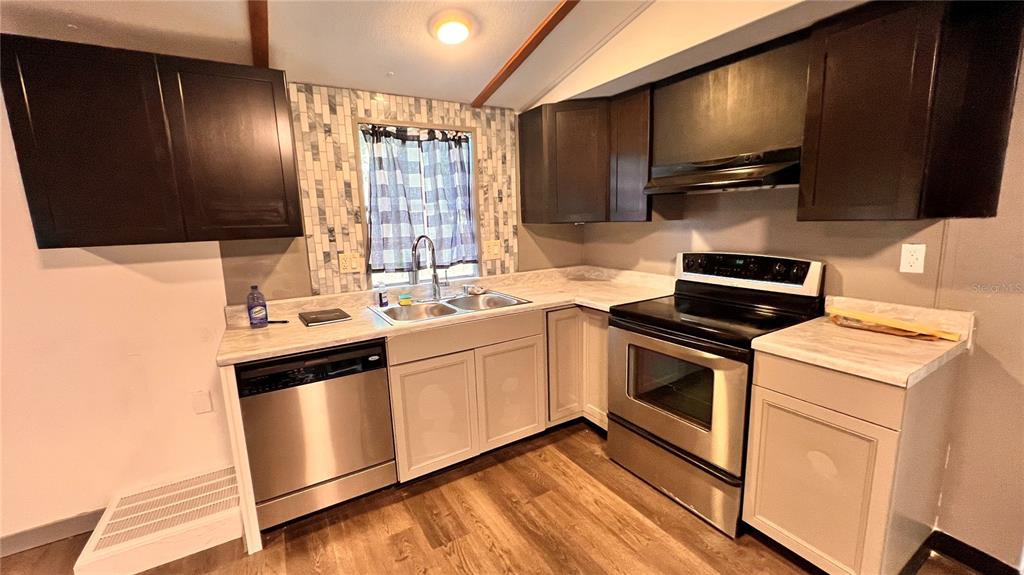 A kitchen features dark upper cabinets, light lower cabinets, stainless steel appliances, and a tiled backsplash — 4228 ATHENS AVENUE, NEW PORT RICHEY, FL