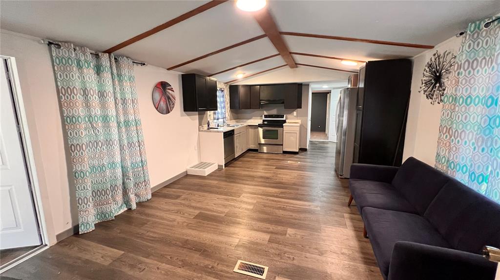 An open-concept kitchen and living area features dark cabinets, stainless appliances, and wood-look flooring — 4228 ATHENS AVENUE, NEW PORT RICHEY, FL