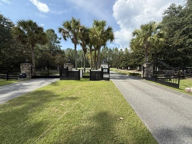 A paved driveway leads through an open black metal gate flanked by stone pillars and palms — 0 NW 148 LANE, REDDICK, FL