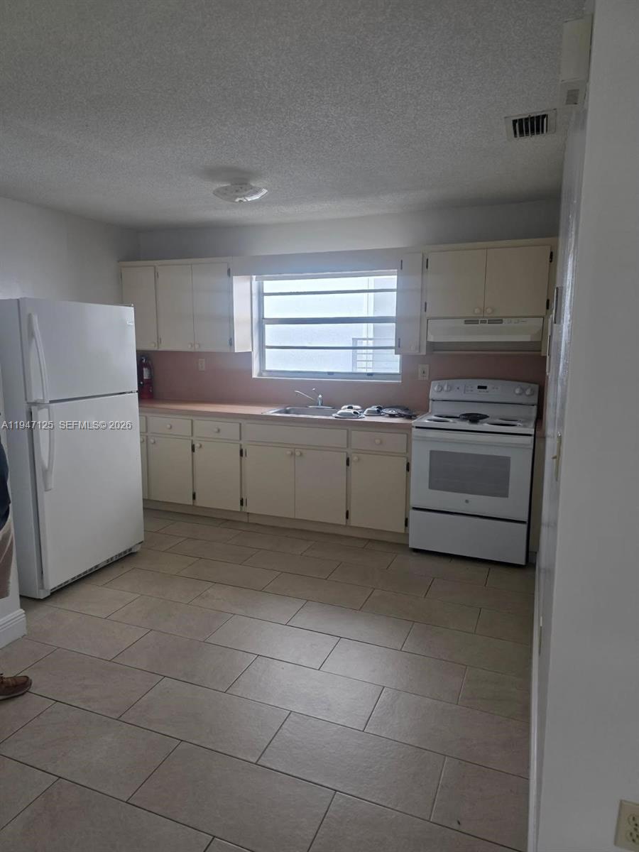 A kitchen with white appliances, light-colored cabinets, a window above the sink, and tiled floors — 1575 NW 1st ST # 3, Miami FL 33125, MIAMI, FL
