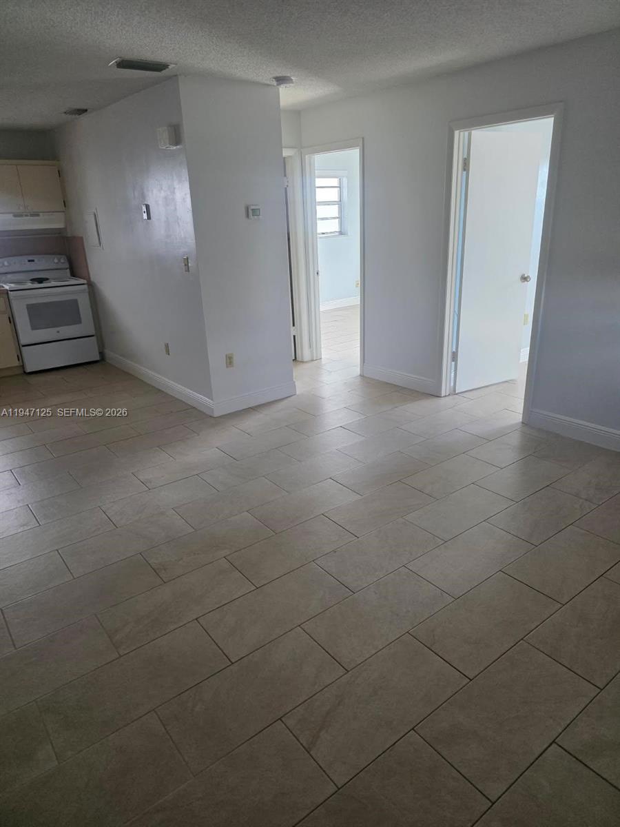 A kitchen area with a white stove leads to two doorways in a tiled room — 1575 NW 1st ST # 3, Miami FL 33125, MIAMI, FL