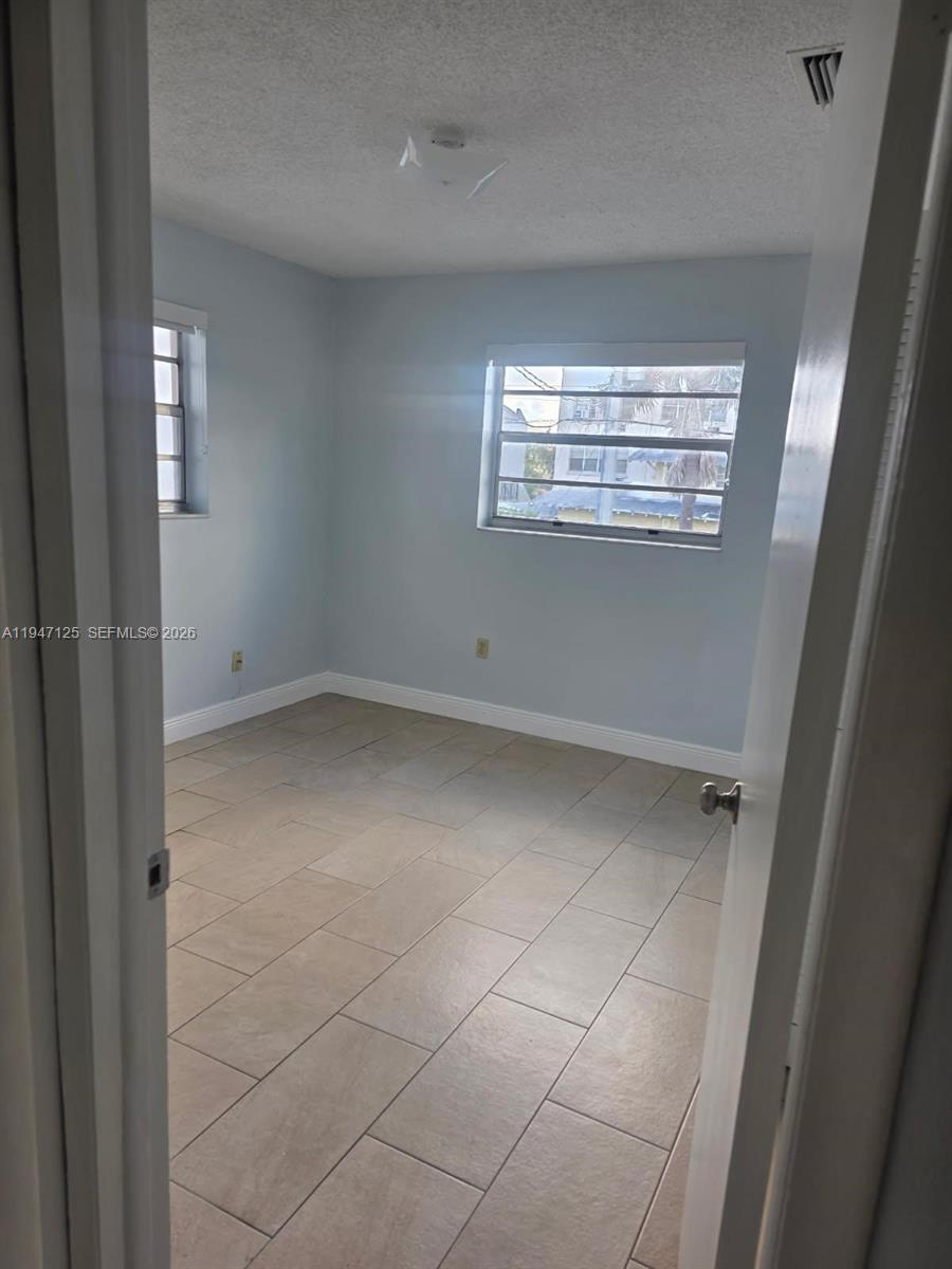 An empty bedroom features light blue walls, beige tile flooring, and two windows — 1575 NW 1st ST # 3, Miami FL 33125, MIAMI, FL