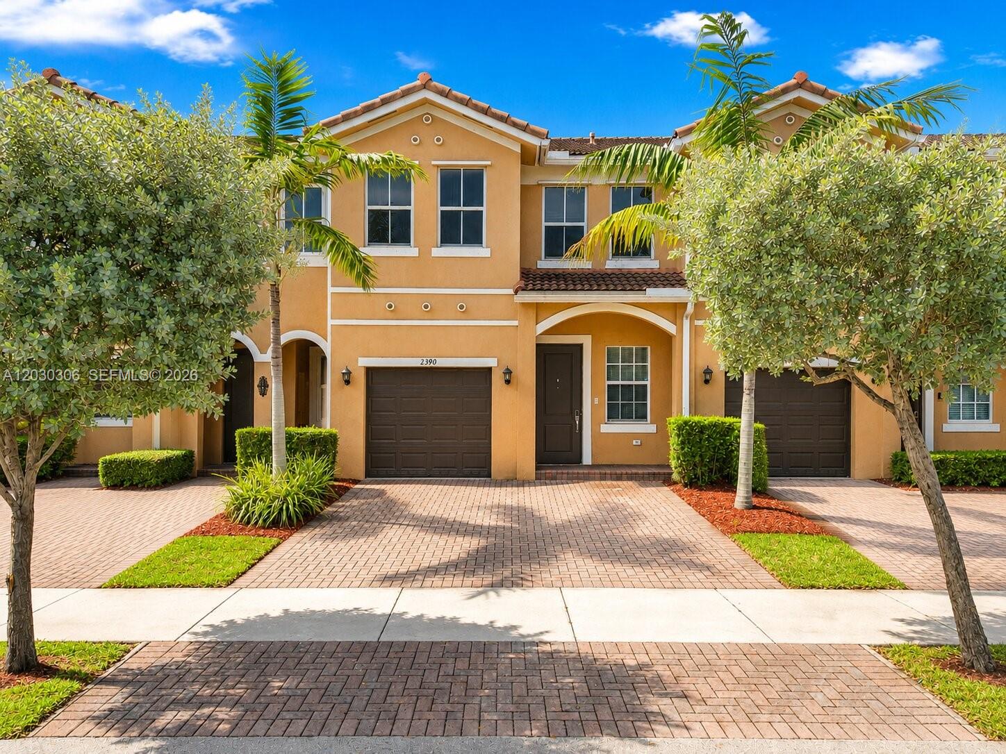 A two-story tan townhouse with a brick driveway, two garages, and palm trees in front — 2390 SE 15th St, Homestead FL 33035, HOMESTEAD, FL