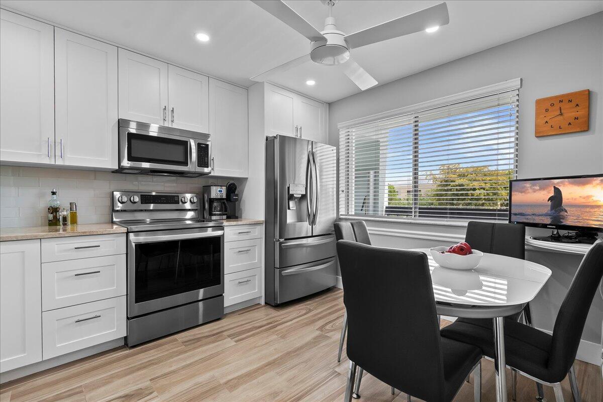 A modern kitchen features white cabinetry, stainless steel appliances, and a small dining area — 6698 10th Avenue N # 305, Lake Worth FL 33461, LAKE WORTH, FL