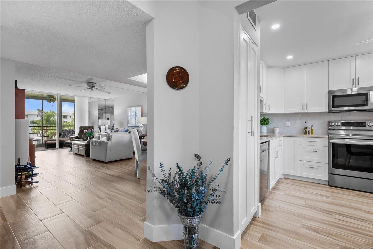 A view from a tiled hallway into a bright kitchen and an adjacent living area — 6698 10th Avenue N # 305, Lake Worth FL 33461, LAKE WORTH, FL