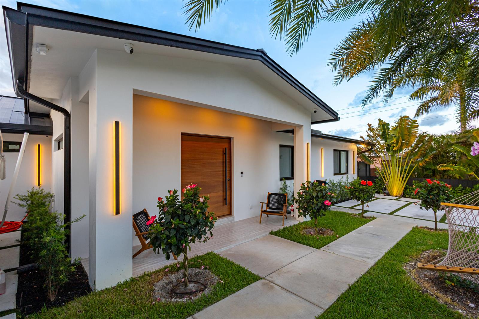 A modern white house exterior features a wooden front door, linear wall lights, and landscaping — 807 Hollywood Place, West Palm Beach FL 33405, WEST PALM BEACH, FL