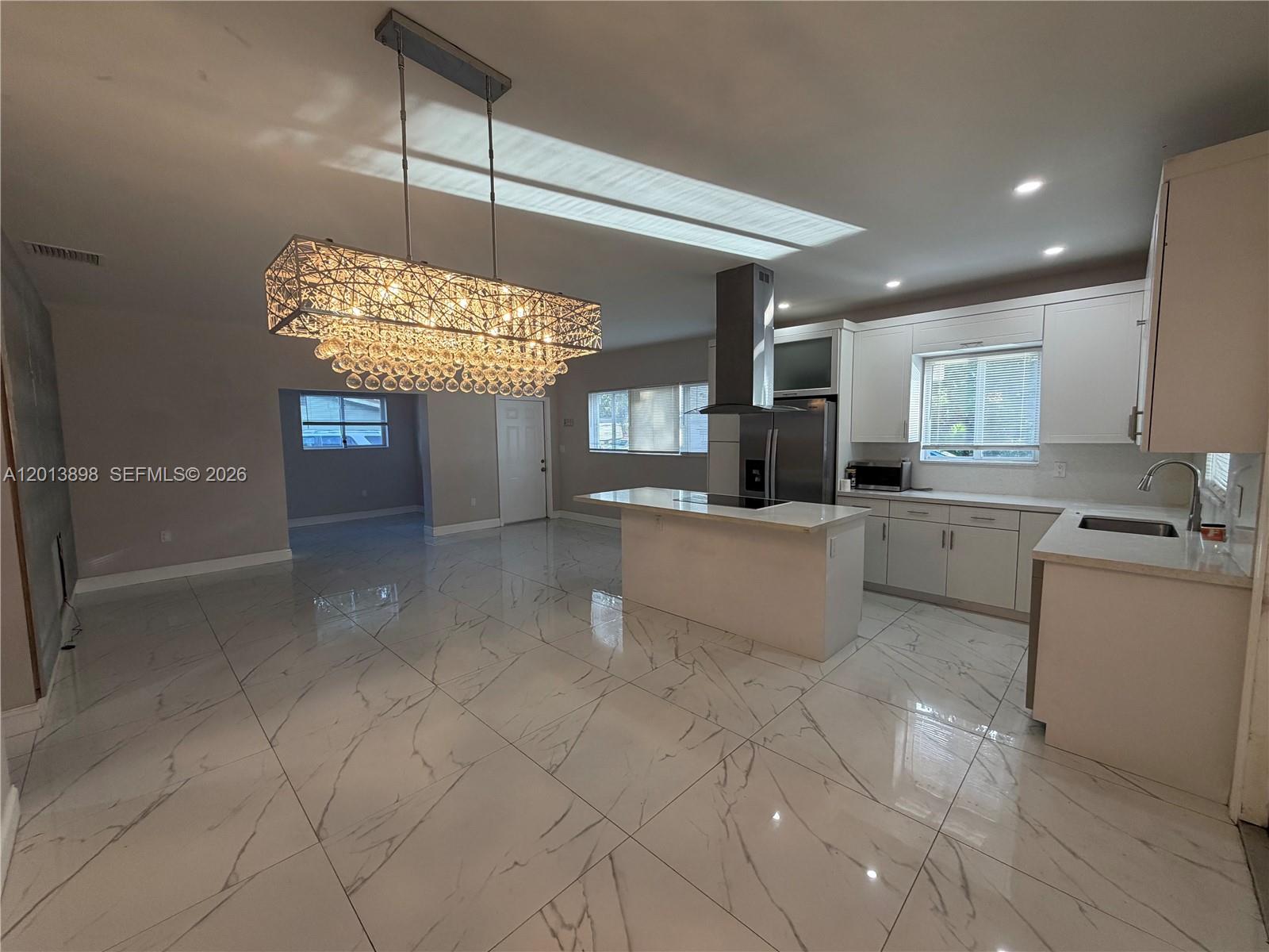 A modern kitchen features white cabinetry, a central island, and large marble-patterned floor tiles — 2241 N 62nd Ave, Hollywood FL 33024, HOLLYWOOD, FL