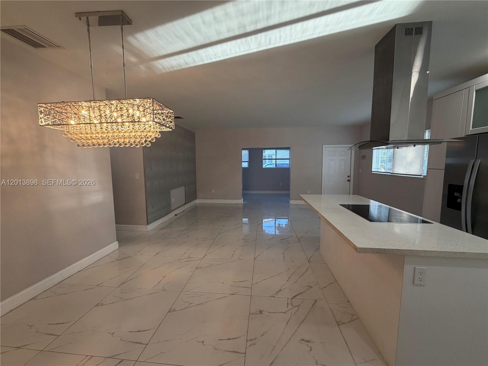 A modern kitchen features a large island, stainless steel range hood, and white marble-look flooring — 2241 N 62nd Ave, Hollywood FL 33024, HOLLYWOOD, FL