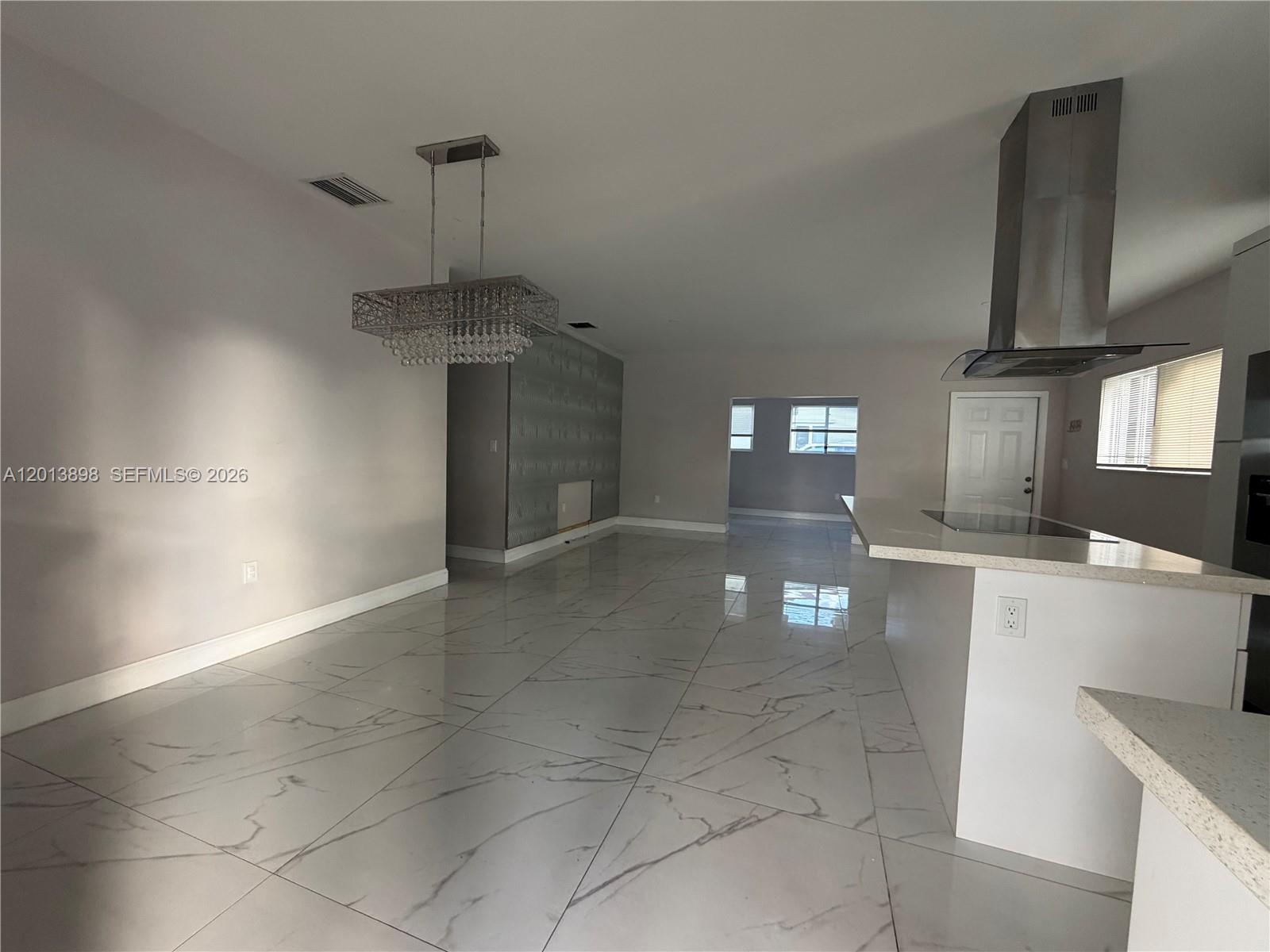 A modern kitchen and dining area feature white marble-look tile floors and a crystal chandelier — 2241 N 62nd Ave, Hollywood FL 33024, HOLLYWOOD, FL