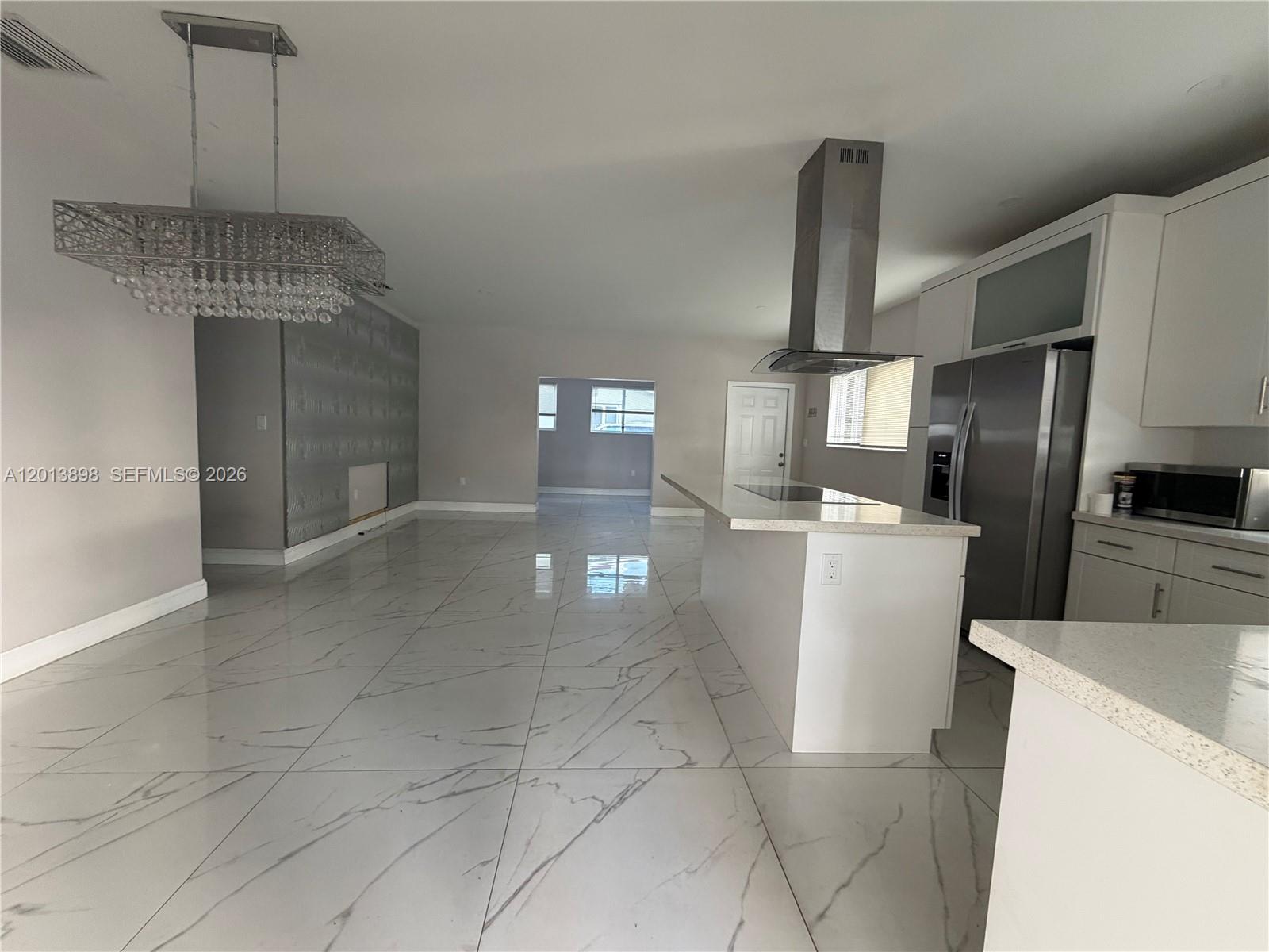 A modern kitchen and living area feature white marble-style tile flooring and a crystal chandelier — 2241 N 62nd Ave, Hollywood FL 33024, HOLLYWOOD, FL