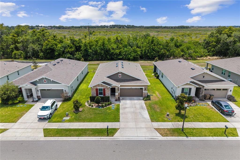 An aerial view shows three suburban houses with driveways and lawns facing a grassy field — 10200 SPRING LAKE DRIVE, CLERMONT, FL