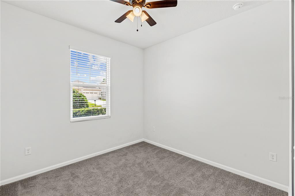An empty bedroom features gray carpet, white walls, a ceiling fan, and a single window — 10200 SPRING LAKE DRIVE, CLERMONT, FL