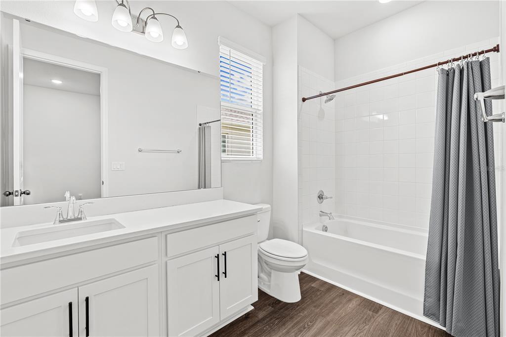 A bathroom features a white vanity, a toilet, and a shower-tub combination with white tiles — 10200 SPRING LAKE DRIVE, CLERMONT, FL