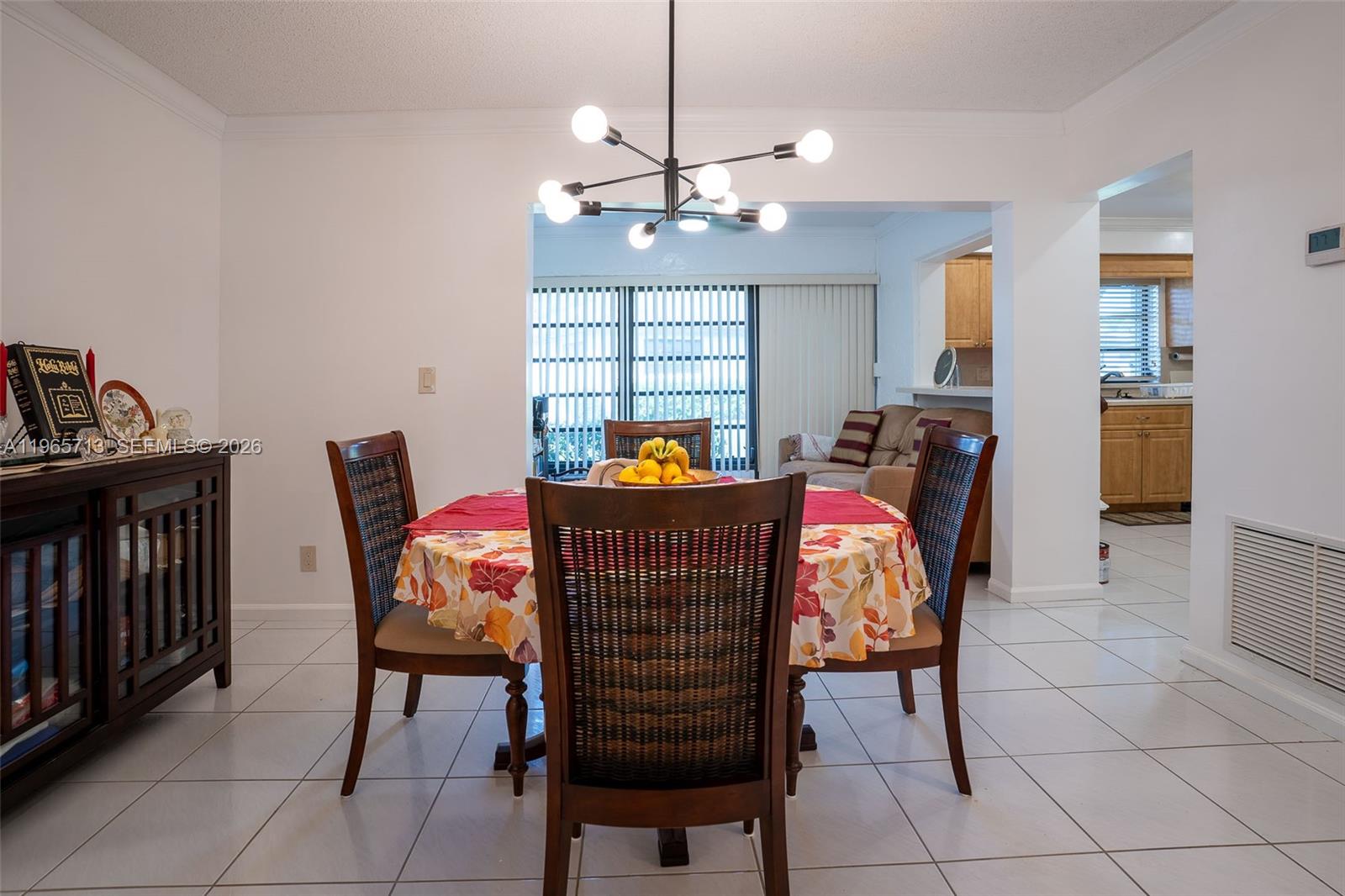 A dining area features a round table with chairs, a modern chandelier, and tiled floors — 10198 DOVEWOOD LN # A, Boynton Beach FL 33436, BOYNTON BEACH, FL