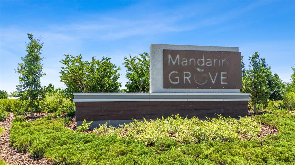 A neighborhood entrance sign for Mandarin Grove stands in a landscaped garden under blue skies — 3808 109TH STREET E, PALMETTO, FL