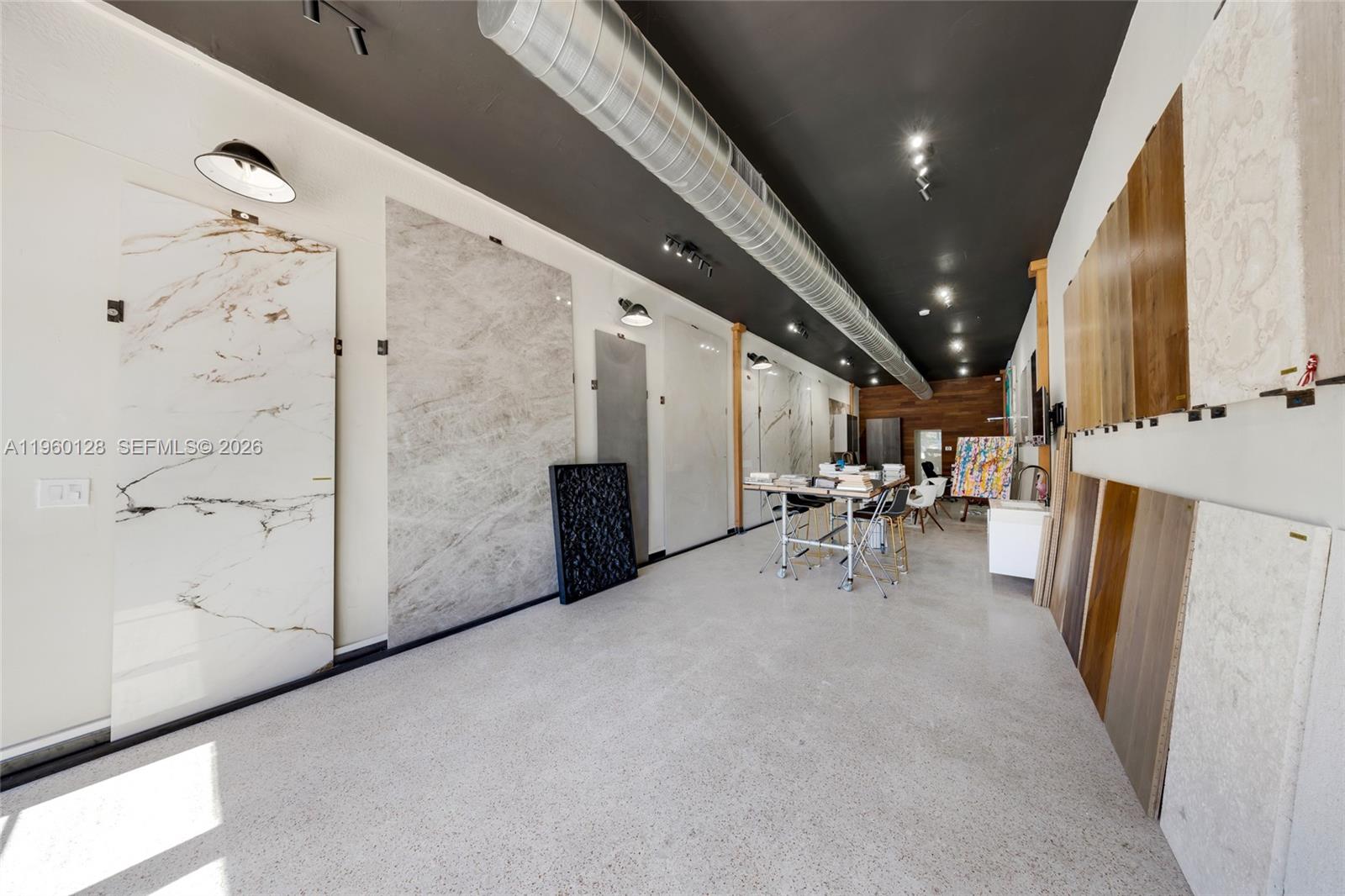 A showroom displays large stone slabs and wood flooring samples under a black industrial ceiling — 1975 71st St, Miami Beach FL 33141, MIAMI BEACH, FL