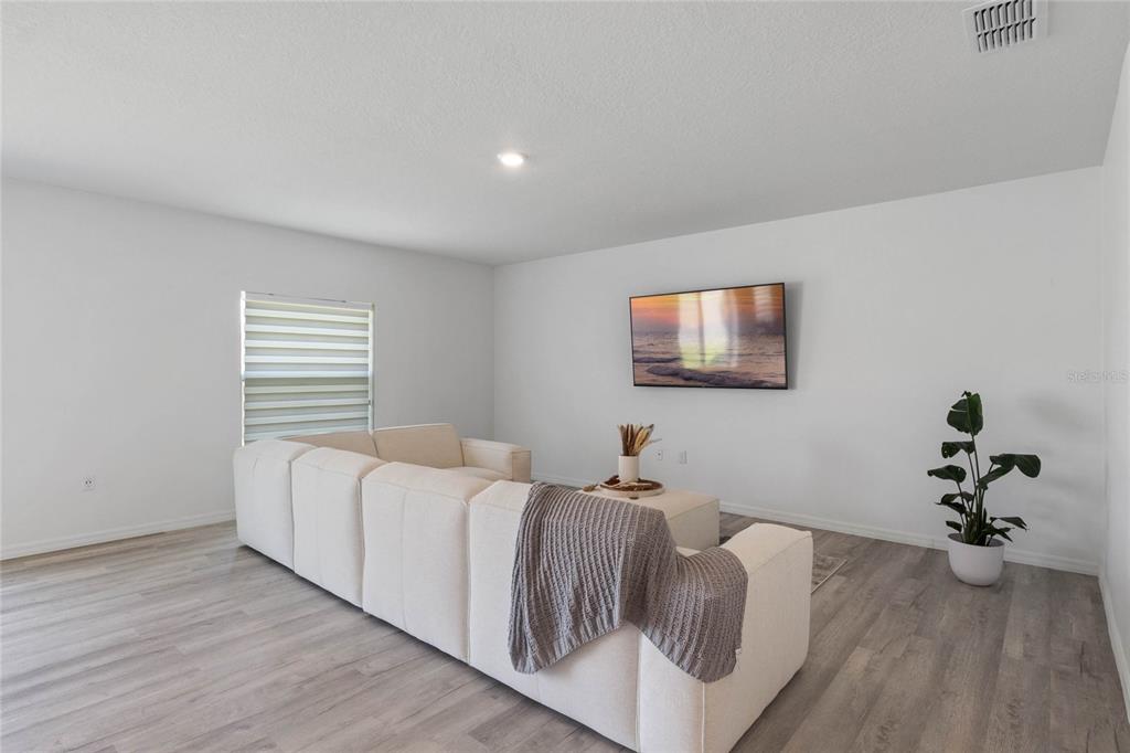 A living room features light wood-look flooring, a white sectional sofa, and a wall-mounted television — 470 HAMLET LOOP, DAVENPORT, FL