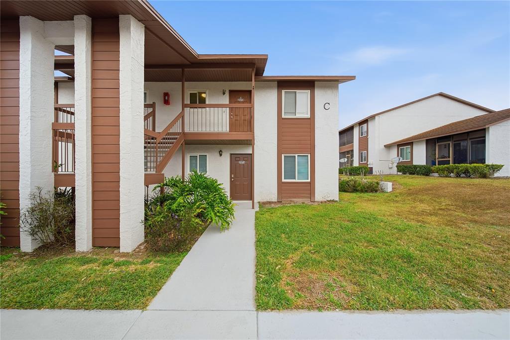 A two-story apartment building with brown trim, white stucco walls, and an exterior staircase — 39132 COUNTY ROAD 54 UNIT 2076, ZEPHYRHILLS, FL