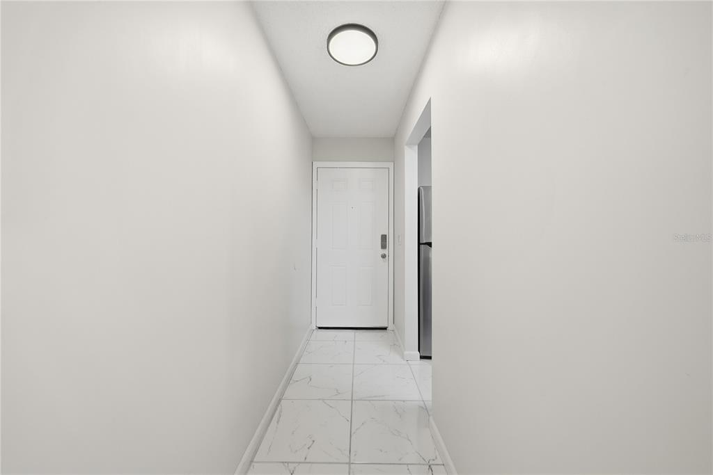 A narrow hallway with white walls, white marble-look tile flooring, and a white entry door — 39132 COUNTY ROAD 54 UNIT 2076, ZEPHYRHILLS, FL