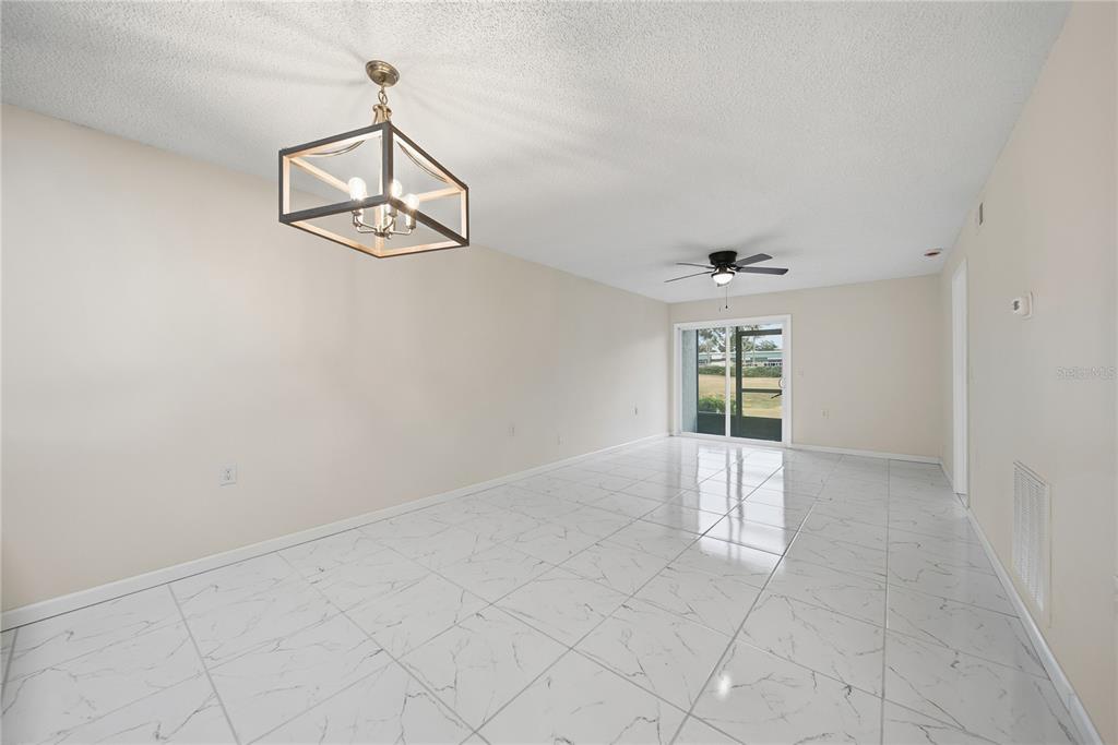 An empty dining area features white marble-look tile flooring, a geometric chandelier, and sliding glass doors — 39132 COUNTY ROAD 54 UNIT 2076, ZEPHYRHILLS, FL