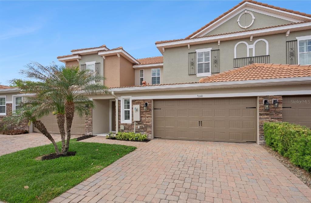 A two-story townhouse exterior features a stone-accented facade, a paved driveway, and a garage — 5640 SIRACUSA LANE, SANFORD, FL