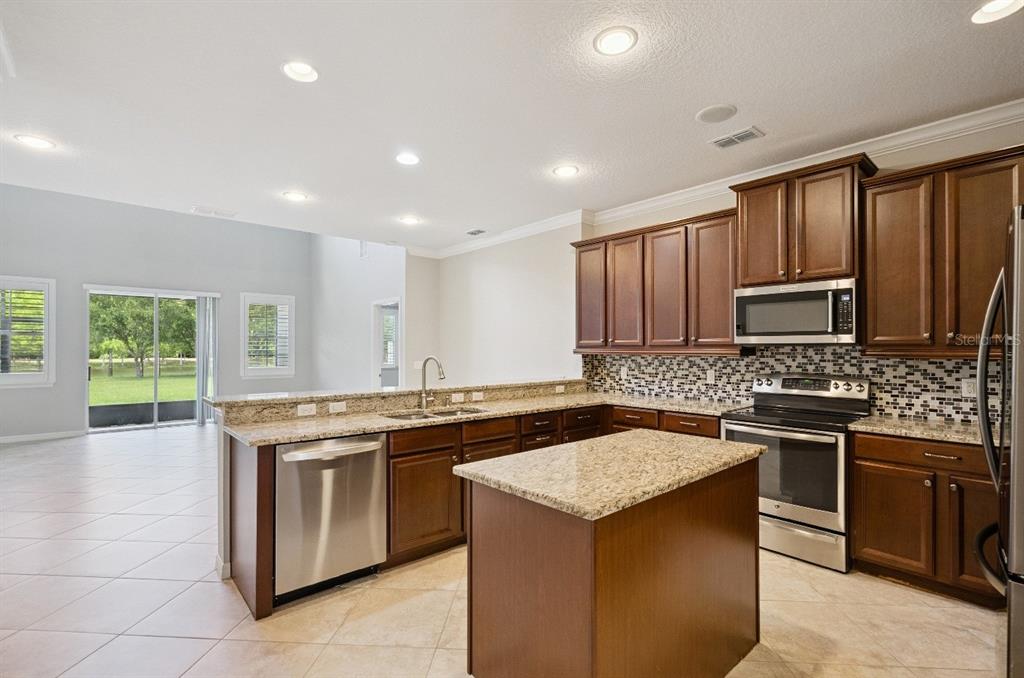A kitchen with dark wood cabinets, granite countertops, stainless steel appliances, and a center island — 5640 SIRACUSA LANE, SANFORD, FL
