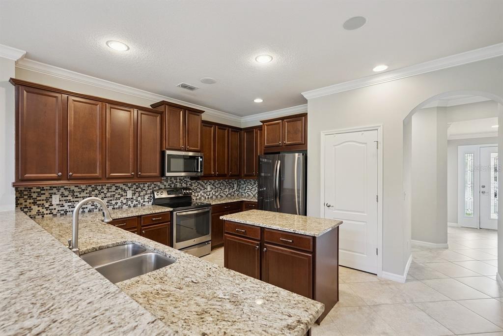 A kitchen features dark wood cabinets, granite countertops, a center island, and stainless steel appliances — 5640 SIRACUSA LANE, SANFORD, FL