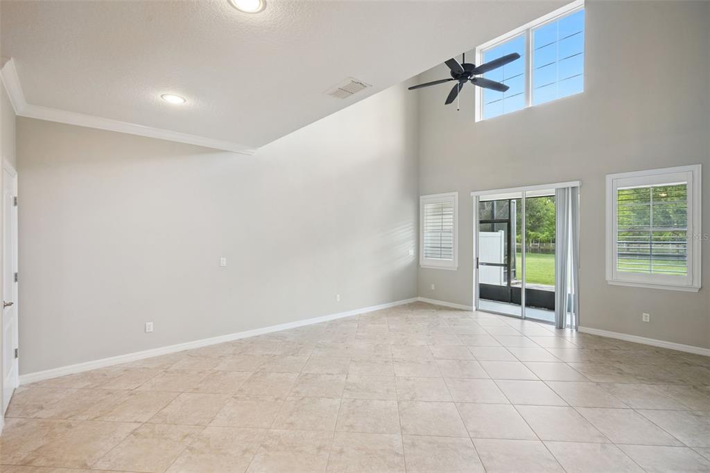 A spacious living room with high ceilings, tile flooring, a ceiling fan, and sliding doors — 5640 SIRACUSA LANE, SANFORD, FL