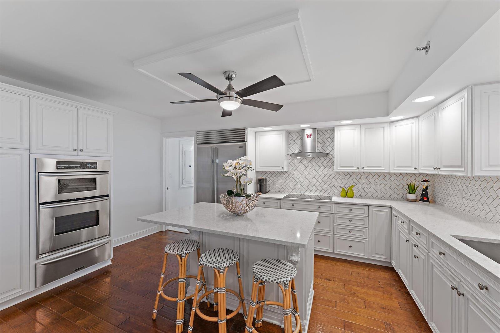 A white kitchen features a central island, stainless steel appliances, and dark wood flooring — 19670 Beach Road # B303, Jupiter FL 33469, JUPITER, FL