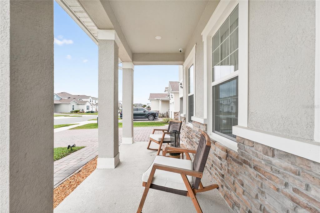 A covered front porch features two wooden chairs, stone siding, and square support columns — 19076 PLANETREE STREET, ORLANDO, FL