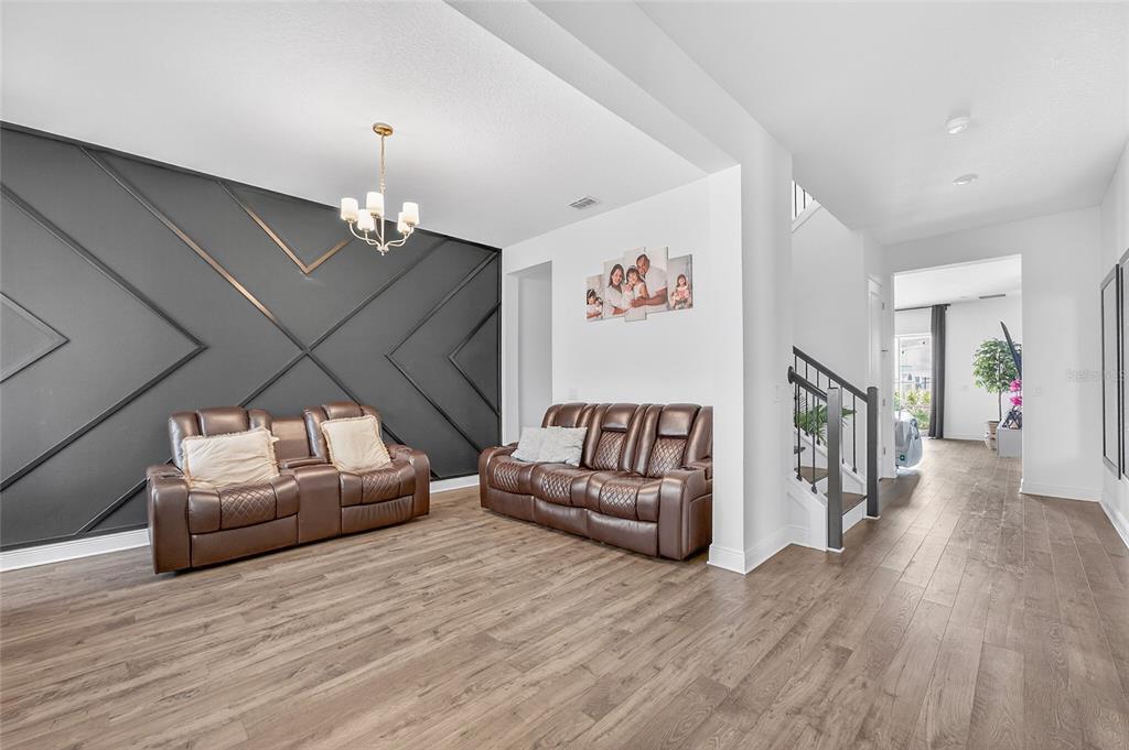 A living room features a dark accent wall with geometric molding, brown leather sofas, and wood-look flooring — 19076 PLANETREE STREET, ORLANDO, FL