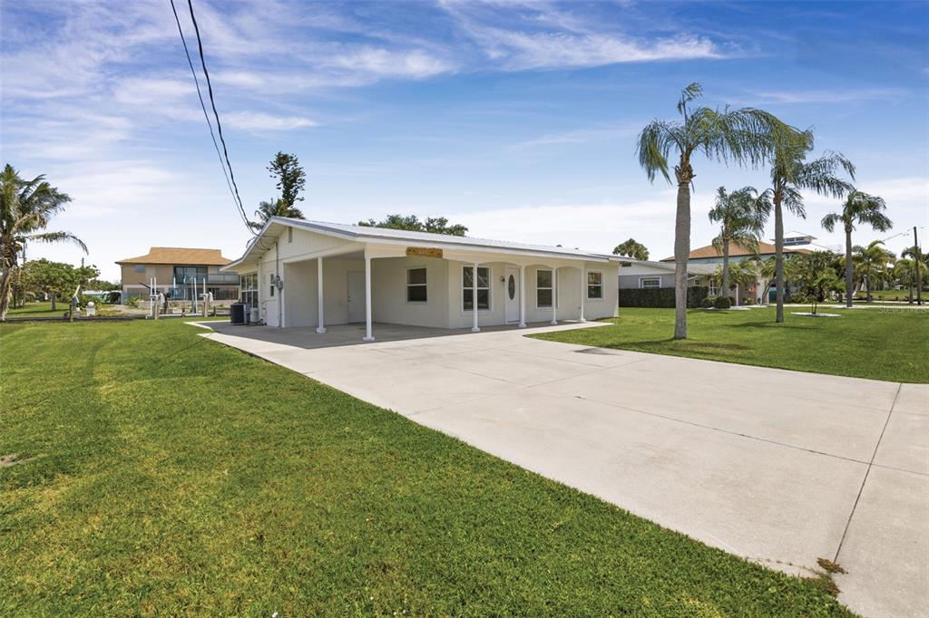 A single-story white house with a carport and a large concrete driveway on a lawn — 10451 MARION STREET, ENGLEWOOD, FL