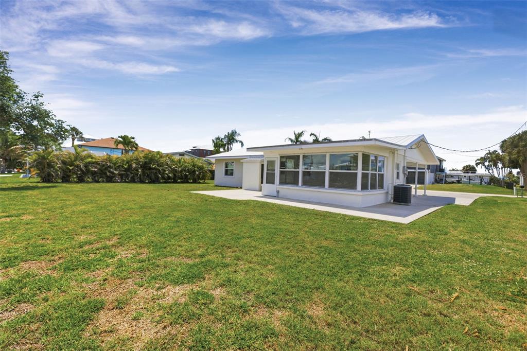 A white house with a large sunroom sits on a grassy lot under a sky — 10451 MARION STREET, ENGLEWOOD, FL